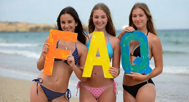 FAQ LISA! Sprachreisen Mallorca Premium – Antworten für Young Adults zu Sprachreisen Young Adults am Strand in Mallorca halten FAQ Buchstaben während einer LISA! Sprachreise mit Meer im Hintergrund