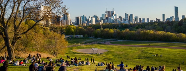 Viele Menschen entspannen in der Abendsonne im Park mit Blick auf die Skyline von Toronto
