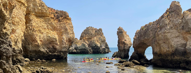 Zwischen Felsen im Meer paddeln Boote hindurch bei einer Sprachreise in Faro