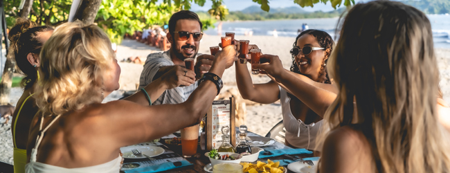 Gemeinsames Essen am Strand von Sámara in Costa Rica Mehrere Erwachsene sitzen am Strand und essen und trinken gemeinsam