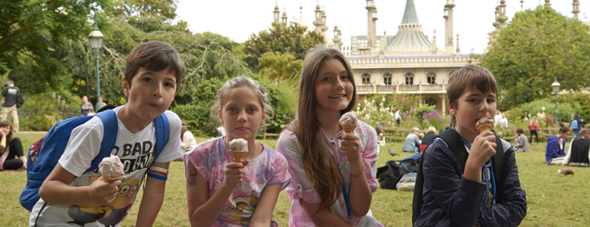 Vier Kinder sitzen vor dem Royal Pavillion in Brighton im Grünen und essen ein Eis