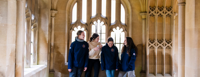Vier Mädchen unterhalten sich in einem mittelalterliche aussehenden Gang in Cheltenham Collge