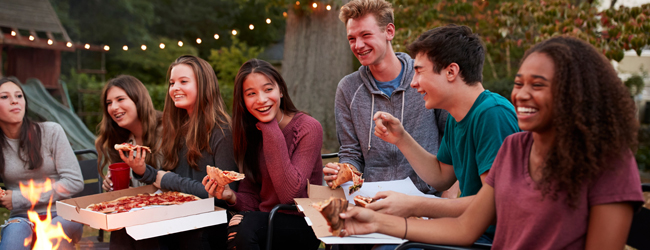 Jugendliche sitzen am Abend am Lagerfeuer und essen Pizza